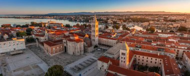 Zadar, Croatia - Aerial panoramic view of the Forum of the old town of Zadar with the Church of St. Donatus and the bell tower of the Cathedral of St. Anastasia on a summer morning with golden sunrise clipart