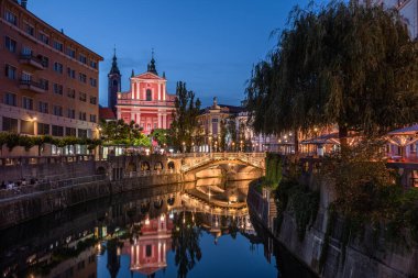 Ljubljana, Slovenya - Slovenya 'nın başkenti Ljubljana' nın Ljubljana kentinde, bir yaz gecesi mavi saatte aydınlatılmış Tromostovje köprüsü ve Fransisken Annunciation Kilisesi