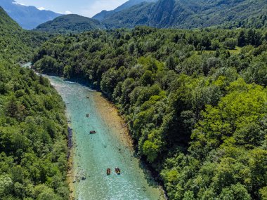 Soca Vadisi, Slovenya - Parlak güneşli bir yaz gününde yeşil yapraklarla nehirden geçen zümrüt alp nehri manzaralı Soca kanoları ve rafting tekneleri