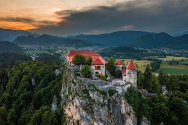 Bled, Slovenya - arka planda Julian Alpleri üzerinde dramatik altın gün batımı gökyüzü ile güzel Kanlı Kale 'nin (Blejski Grad) havadan görünüşü