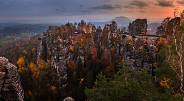 Sakson, Almanya - Bastei köprüsünün panoramik manzarası güneşli bir sonbahar günbatımı renkli yapraklar ve gökyüzü. Bastei, Dresden yakınlarındaki Sakson İsviçre Ulusal Parkı 'ndaki güzel kaya oluşumuyla ünlüdür.