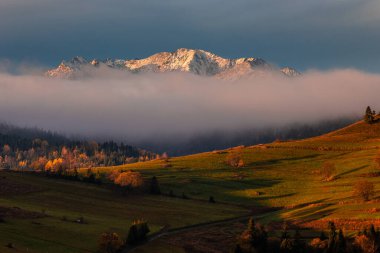 Osturna, Slovakya - Güneşli bir sonbahar sabahında yüksek Tatras dağlarının panoramik manzarası ve arka planda sıcak altın gündoğumu renkleri ve sisli dağlar. Gün doğumu ışıkları, mavi gökyüzü