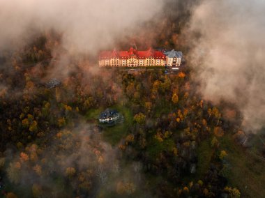 Tatrzanska Lomnica, Slovakia - Aerial view of beautiful warm colorful forest at a hotel by the High Tatras with golden autumn foliage and foggy mountains at sunset clipart