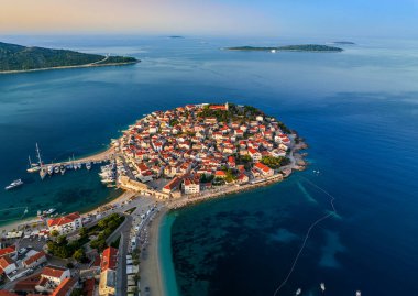 Primosten, Hırvatistan - Hırvatistan 'ın başkenti Primosten yarımadasının havadan görünüşü, St. George Kilisesi, Hırvatistan' ın Dalmaçya kentinde güneşli bir yaz sabahı eski bir kasaba. Altın ve mavi gökyüzü, yat marinası ve turkuaz deniz suyu gün doğumunda.