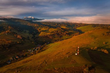 Osturna, Slovakya - Yüksek Tatras Dağları 'nın panoramik manzarası güneşli bir sonbahar sabahında yeşillik, radyo kulesi ve arka planda sisli dağlarla sıcak altın gündoğumu renkleriyle