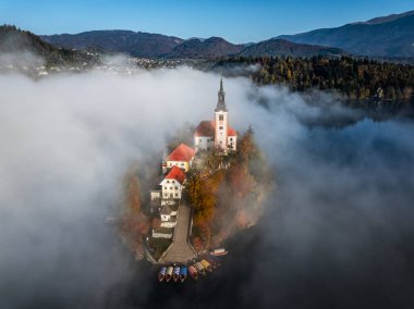 Bled, Slovenia - Aerial view of beautiful Lake Bled (Blejsko Jezero) with Pilgrimage Church of the Assumption of Maria on a small island with Pletna boats and fog over the lake on an autumn morning clipart