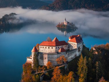 Bled, Slovenya - Bled Gölü (Blejsko Jezero), sisli bir sonbahar sabahı arka planda Maria ve Julian Alps Hükmü Kilisesi ile güzel Bled Kalesi 'nin (Blejski Grad) havadan görünüşü