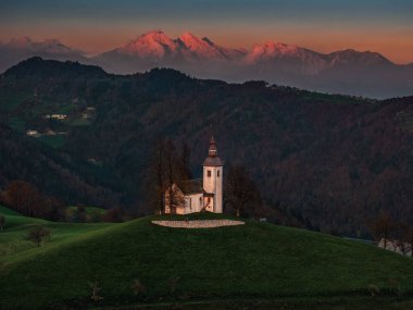 Skofja Loka, Slovenya - Sveti Tomaz 'ın (Saint Thomas) güzel tepe kilisesinin havadan görünüşü, Julian Alps' in arka planda parlayan günbatımı renkleriyle Ekim, sonbaharda
