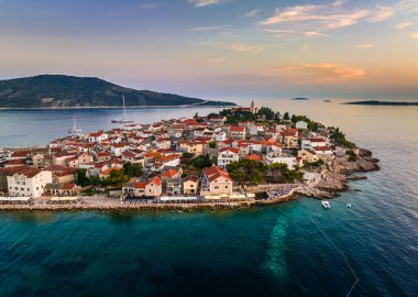 Primosten, Hırvatistan - Hırvatistan 'ın Dalmaçya kentinde güneşli bir yaz öğleden sonrasında Primosten yarımadası ve eski kentin havadan manzarası. Yatlar, Adriyatik kıyılarında gün batımında mavi ve altın rengi gökyüzü