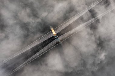 Budapest, Hungary - Aerial view of one of the pillars of the Megyeri Bridge over River Danube on a foggy autumn afternoon with heavy autumn fog bellow and golden shine on the pillar clipart