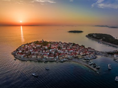 Primosten, Hırvatistan - Dalmaçya 'da güneşli bir yaz öğleden sonrasında Primosten yarımadası ve eski kasabanın havadan panoramik manzarası. Yat marinası, yelkenliler, batan güneş, Adriyatik kıyılarında gün batımında altın gökyüzü.