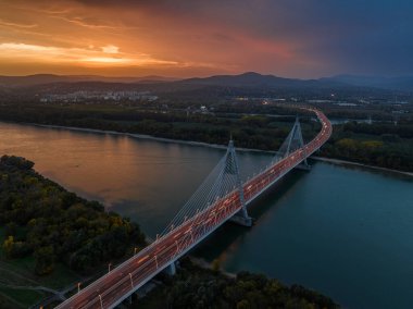 Budapeşte, Macaristan - Tuna Nehri üzerindeki Megyeri Köprüsü 'nün havadan görünüşü alacakaranlıkta dramatik altın gün batımı gökyüzü ve arkada Buda Tepeleri