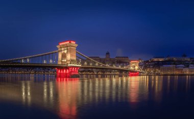 Budapeşte, Macaristan - Budin Sarayı 'nın arka planında karlı Buda Tepeleri ve çatılarıyla bir kış akşamında Szechenyi Zinciri Köprüsü' nü aydınlatmıştır.