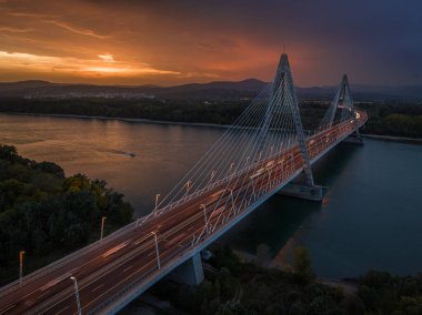 Budapeşte, Macaristan - Tuna Nehri üzerindeki Megyeri Köprüsü 'nün havadan görünüşü alacakaranlıkta dramatik altın gün batımı gökyüzü ve arkada Buda Tepeleri