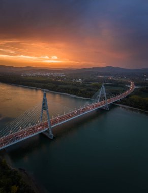 Budapeşte, Macaristan - Tuna Nehri üzerindeki Megyeri Köprüsü 'nün havadan dikey panoramik görüntüsü ve arka planda dramatik altın gün batımı gökyüzü ve Buda Tepeleri