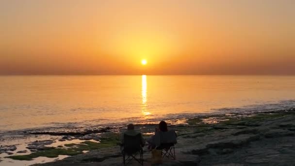 Κόσμος Κάθεται Στην Παραλία Και Βλέπει Ηλιοβασίλεμα — Αρχείο Βίντεο