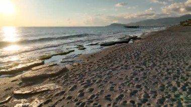 Sarı paltolu bir kız sahilde yürüyor.