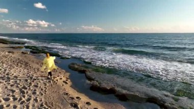 Sarı paltolu bir kız sahilde yürüyor.