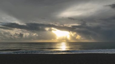 Okyanus dalgaları su sıçratıyor ve beyaz köpük oluşturuyor, kumlu sahile vuruyor. Tropik