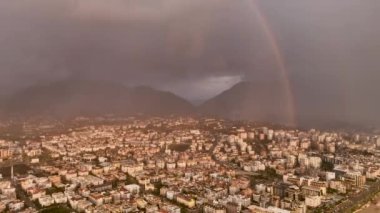 Strong rainbow above the city skyline over the houses and buildings in the daytime. The vivid phenomenon of nature. 4K