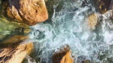 The water is rushing along colorful stones aerial view 4K flowing in the deep lake