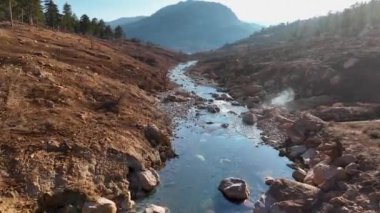 The water is rushing along colorful stones aerial view 4K flowing in the deep lake