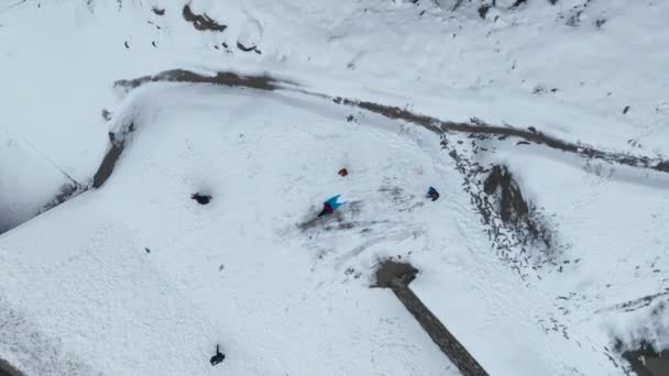 雪の滑り台の上の陽気な子供 冬に白い丘から滑り降りるプラスチック製のそりに乗っている小さな男の子 冬休みを楽しんでいるかわいい子供 — ストック動画