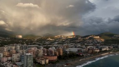 Yazın yağmurdan sonra hava manzarası. Şehrin yerleşim yerindeki çok katlı binaların üzerinde gökkuşağı. 4K