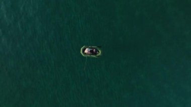 Temiz deniz yüzeyinde şişme lastik teknede yüzen genç adamın hava görüntüsü..