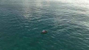 Temiz deniz yüzeyinde şişme lastik teknede yüzen genç adamın hava görüntüsü..