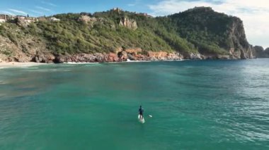 Güneş doğarken SUP panosunda kürek çeken bir adam. Parlayan suda kürek çeken bir adam. Yaz tatili aktivitesi, su sporları..