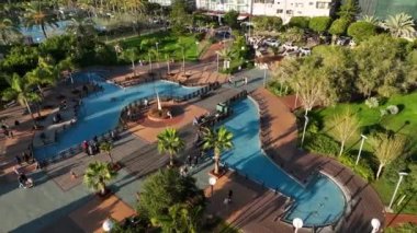 Büyük yeşil palmiye ağaçları olan güzel mavi çeşme insanlar yürüyor ve tatillerinin tadını çıkarıyorlar.