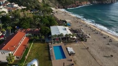 Deniz kıyısındaki terasta gün batımında plajda dinlenen insanlarla dolu restoranın üst manzarası.