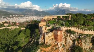 Türkiye 'nin Alanya şehrinde gün batımında dağın tepesindeki eski bir kale, yeşil orman kozalaklı ağaçlarla doludur.