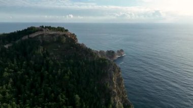 Türkiye 'nin Alanya şehrinde gün batımında dağın tepesindeki eski bir kale, yeşil orman kozalaklı ağaçlarla doludur.