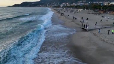 Deniz yüzeyinin yeşil bir kayıktaki deniz sporlarının hava görüntüsü dalgıç kıyafetli bir adam gök mavisi dalgaları yakalar.