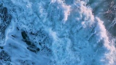 Yavaş çekimde, dev deniz dalgalarının köpüren ve sıçrayan havadan görüntüsü. Güzel su dokusu arka planı, deniz üzerinde güneşli bir gün, drone görüntüleri dalgaları takip ediyor.
