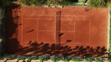 Tenis oyuncuları profesyonel stadyumda maç sırasında hareket halindeler. Hava görüntüsü. Oyuncular turuncu sahada tenis oynuyorlar.