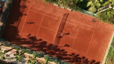 Tenis oyuncuları profesyonel stadyumda maç sırasında hareket halindeler. Hava görüntüsü. Oyuncular turuncu sahada tenis oynuyorlar.