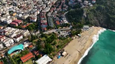 Yukarıdan bakıldığında, turkuaz bir su ile yıkanmış beyaz bir kumsal manzarası ve gevşemiş insanlar.