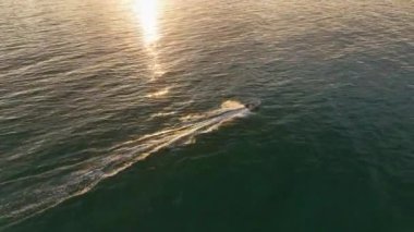 Motorlu aracın turkuaz denizde yelken açtığını gösteren drone görüntüleri. Sakin denizde yüzen sürat teknesi köpüklü dalgalar yaratıyor. Gündüz üst görünüm