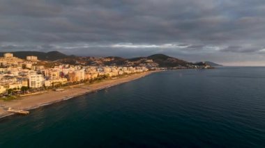 İnsansız hava aracı, oteller, villalar ve diğer evler, bir tatil köyü, kayalık kıyıların doğası ve açık mavi bir Akdeniz koyuyla adanın kıyı bölgesinin fotoğraflarını çekiyor.