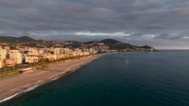 İnsansız hava aracı, oteller, villalar ve diğer evler, bir tatil köyü, kayalık kıyıların doğası ve açık mavi bir Akdeniz koyuyla adanın kıyı bölgesinin fotoğraflarını çekiyor.