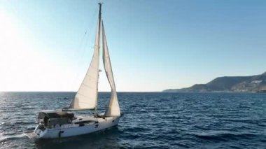 Güneşli bir günde, ufukta mavi denizde yelken açan yat.