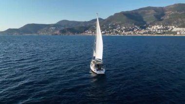 Havadan çekilen görüntüler, açık mavi denizde seyreden lüks yelkenli görüntüsü. Mavi okyanus suyunda yatı takip eden kamera.