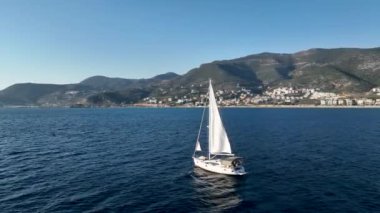 Beyaz yelkenli yat günbatımında turkuaz deniz dalgaları üzerinde yüzer. Hava aracı görüntüleri 4K