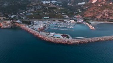Türkiye 'nin Port Alanya kentindeki lüks deniz bölgesinin havadan geniş bir görüntüsü. İHA 'nın kamerası birden fazla yelkenli yatların ve teknelerin üzerinde uçuyor. Yazın alacakaranlıkta limandaki rıhtımda duruyor.