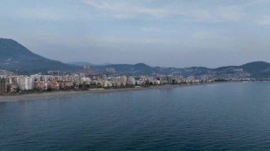 İnsansız hava aracı, oteller, villalar ve diğer evler, bir tatil köyü, kayalık kıyıların doğası ve açık mavi bir Akdeniz koyuyla adanın kıyı bölgesinin fotoğraflarını çekiyor.