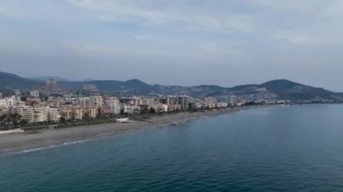 İnsansız hava aracı, oteller, villalar ve diğer evler, bir tatil köyü, kayalık kıyıların doğası ve açık mavi bir Akdeniz koyuyla adanın kıyı bölgesinin fotoğraflarını çekiyor.