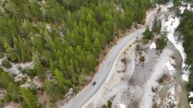 Bir yola bakan hava manzarası, karla kaplı ağaçlar ve karlı ormanın ortasında, karanlık, bulutlu bir kış gününde - tepeden aşağı, drone çekimi